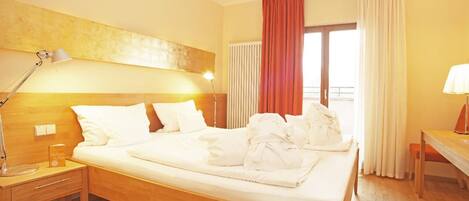 A hotel room with a bed, bedside table, lamp, and a window with curtains.