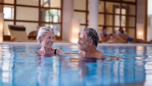 A swimming pool with clear water, surrounded by large windows and indoor seating areas. - Bio Thermalhotel Falkenhof (Bad Fuessing)