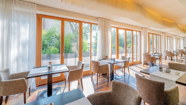 A spacious dining area with large windows, wooden tables, and comfortable chairs. - Bio Thermalhotel Falkenhof (Bad Fuessing)