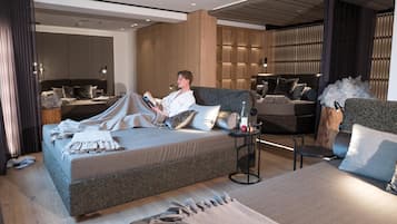 A modern hotel room with a large bed, a sofa, and a small table with a bottle and apple.