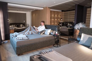 Habitación de hotel moderna con una cama grande, un sofá y una pequeña mesa con una botella y una manzana.