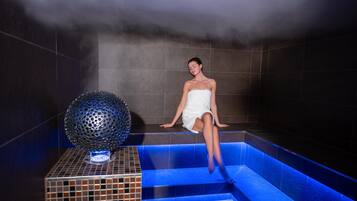 Una persona sentada en una tina de hidromasaje con una fuente iluminada en azul y una esfera decorativa.