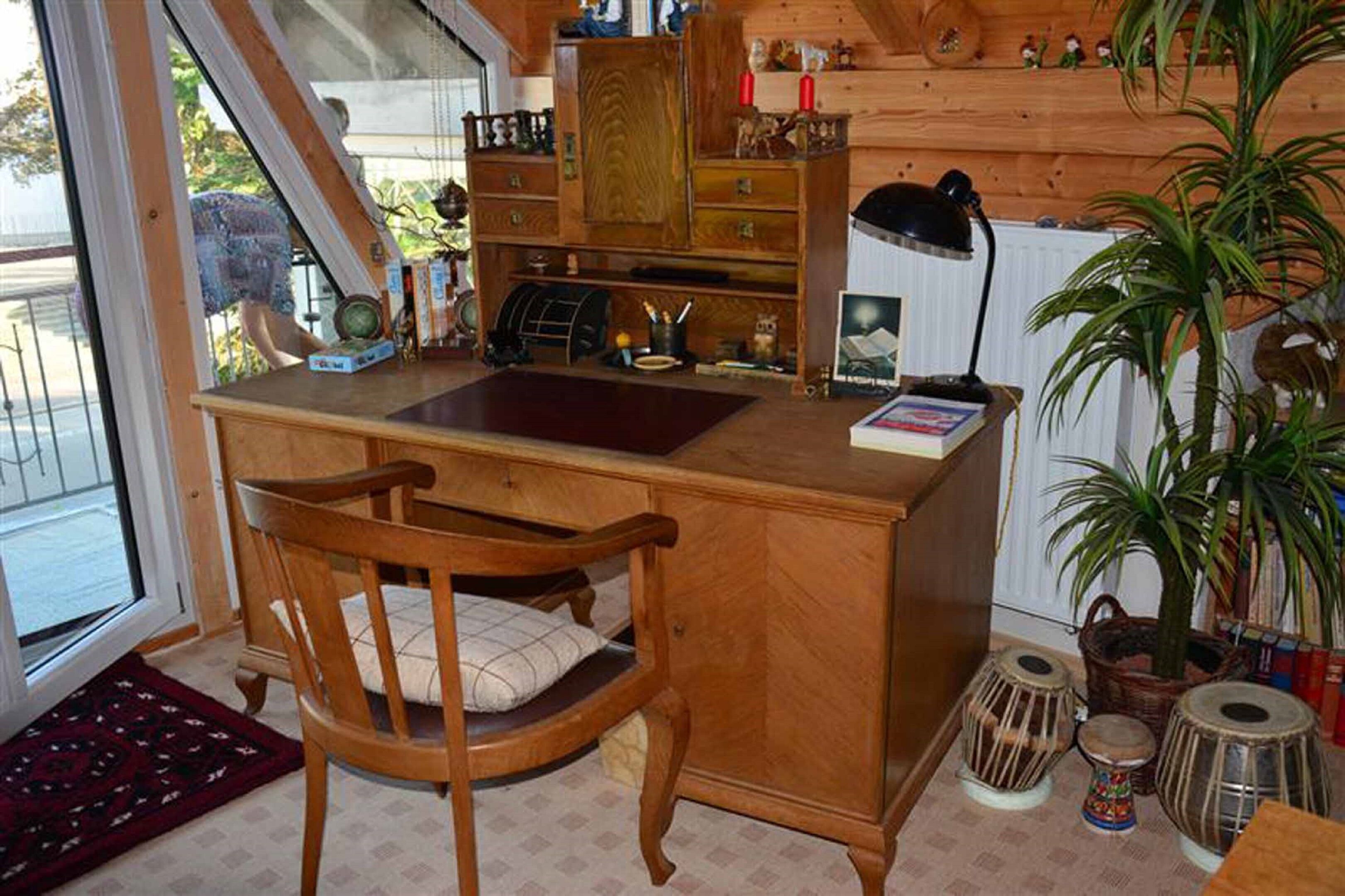A wooden desk with a chair, a small shelf with figurines, a lamp, and a potted plant.