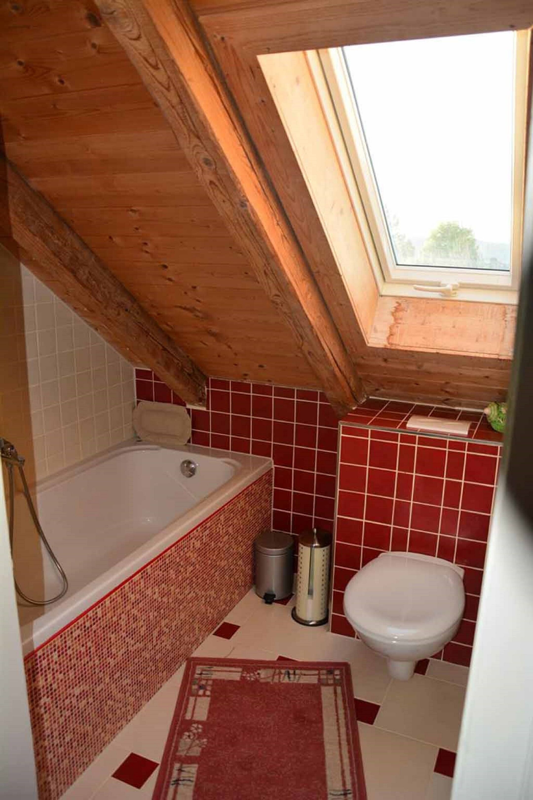 A small bathroom with a skylight, a bathtub, a toilet, and a red-tiled floor.