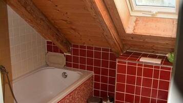 A small bathroom with a skylight, a bathtub, a toilet, and a red-tiled floor.