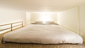 Una cama grande con cabecera de madera, un ventanal pequeño y barandilla de madera.