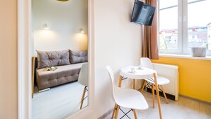 Una habitación moderna con sofá, una mesa de comedor con sillas, un televisor instalado en la pared y una ventana con cortinas.