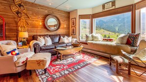 A cozy living room with a wooden wall, a large window with a mountain view, and a variety of seating options. - Amazing Views, free wifi, free parking. Industrial Cozy Telemark Lodge studio (Copper Mountain)