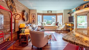 A cozy living room with a wooden wall, a sofa, a red chair, a small table, and a view of the mountains through large windows. - Amazing Views, free wifi, free parking. Industrial Cozy Telemark Lodge studio (Copper Mountain)