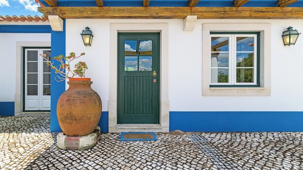 A building with a green door, a window with a white frame, and a large terracotta pot on the ground. - Country House - Quinta das Tílias (Santiago do Cacém)