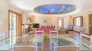 A spacious living room with a glass coffee table, a red floral sofa, and a ceiling mural. - Country House - Quinta das Tílias (Santiago do Cacém)