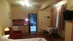Hotellihuone, jossa on sänky, työpöytä, tuoli, pieni pöytä, punainen nojatuoli, keittotila ja televisio.