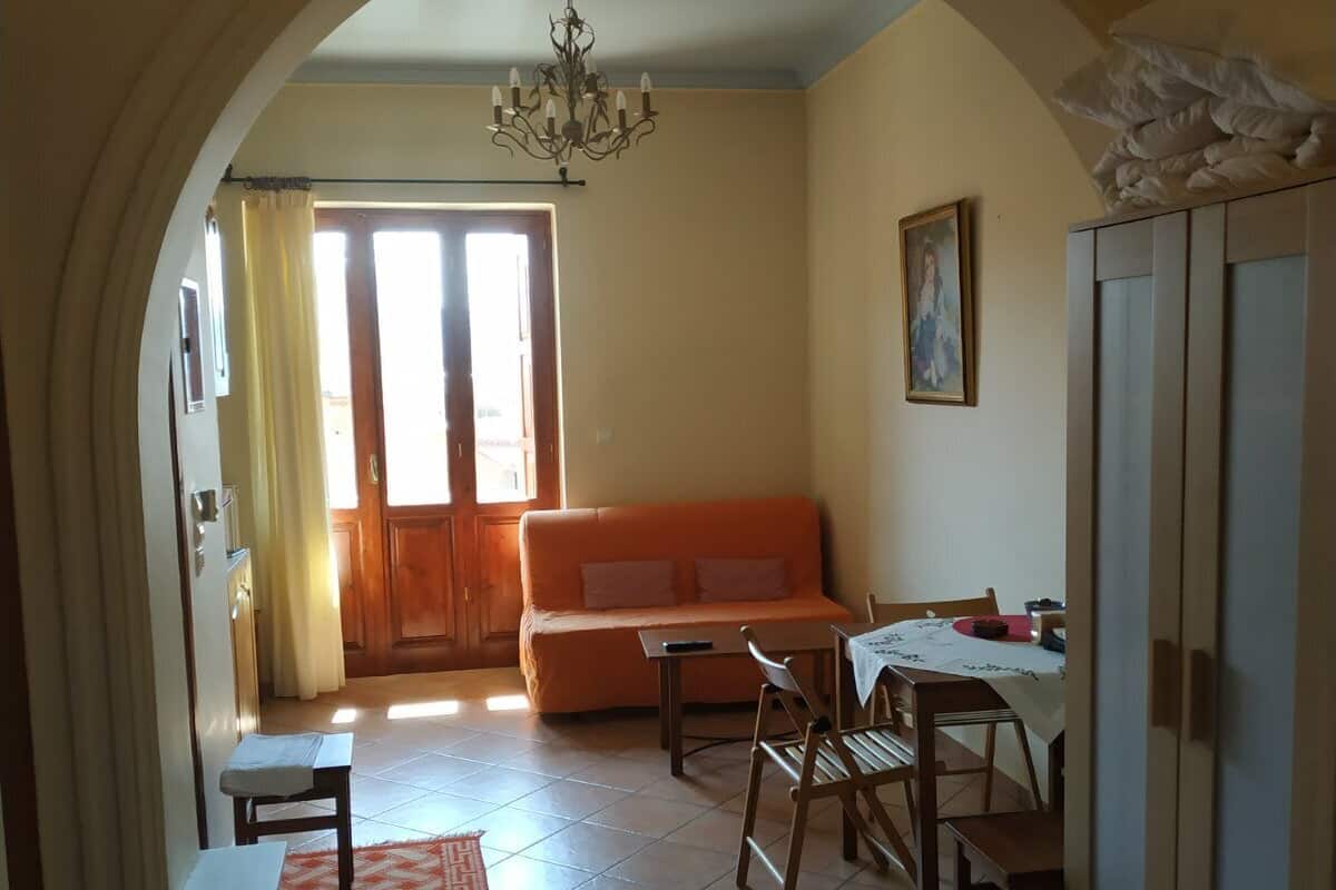 Una sala acogedora con sofá, mesa de comedor, sillas y una araña.
