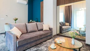 A modern hotel room with a grey sofa, a round wooden coffee table, and a large mirror reflecting the room. - Aparthotel Cracovia Residence (Kraków)