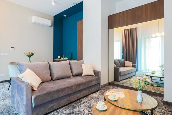A modern hotel room with a grey sofa, a round wooden coffee table, and a large mirror reflecting the room. - Aparthotel Cracovia Residence (Kraków)