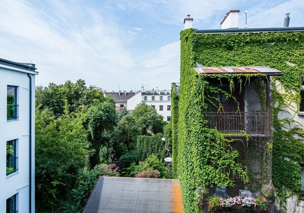 A building with a green ivy-covered exterior, a visible rooftop, and a view of surrounding buildings and trees. - Aparthotel Cracovia Residence (Kraków)