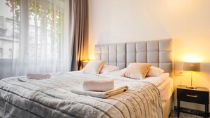 A neatly made bed with a fluffy blanket, two bedside lamps, and a small bedside table. - Aparthotel Cracovia Residence (Kraków)