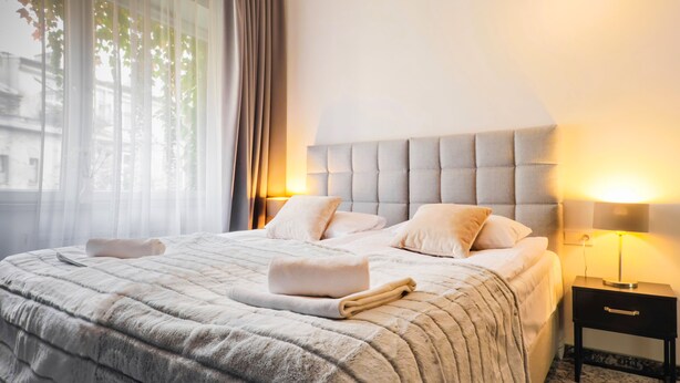 A neatly made bed with a fluffy blanket, two bedside lamps, and a small bedside table. - Aparthotel Cracovia Residence (Kraków)