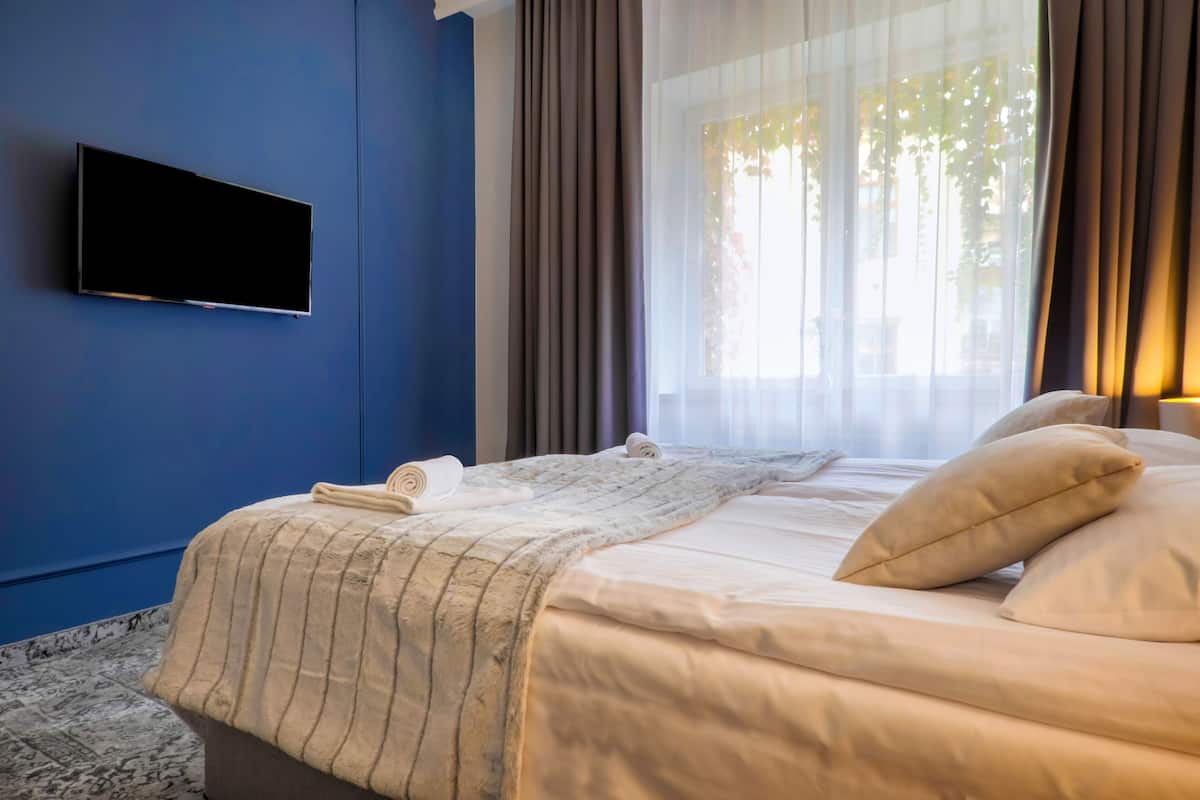 A hotel room with a bed, a flat-screen TV mounted on the wall, and a window with curtains.