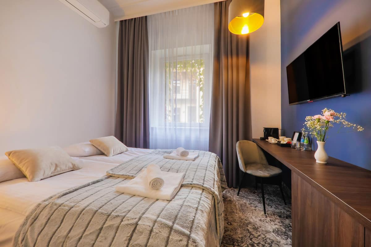 Ein Hotelzimmer mit Bett, Schreibtisch, Stuhl, Fernseher und einem Fenster mit Vorhängen.
