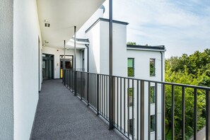 A corridor with a metal railing, white walls, and a view of greenery. - Aparthotel Cracovia Residence (Kraków)