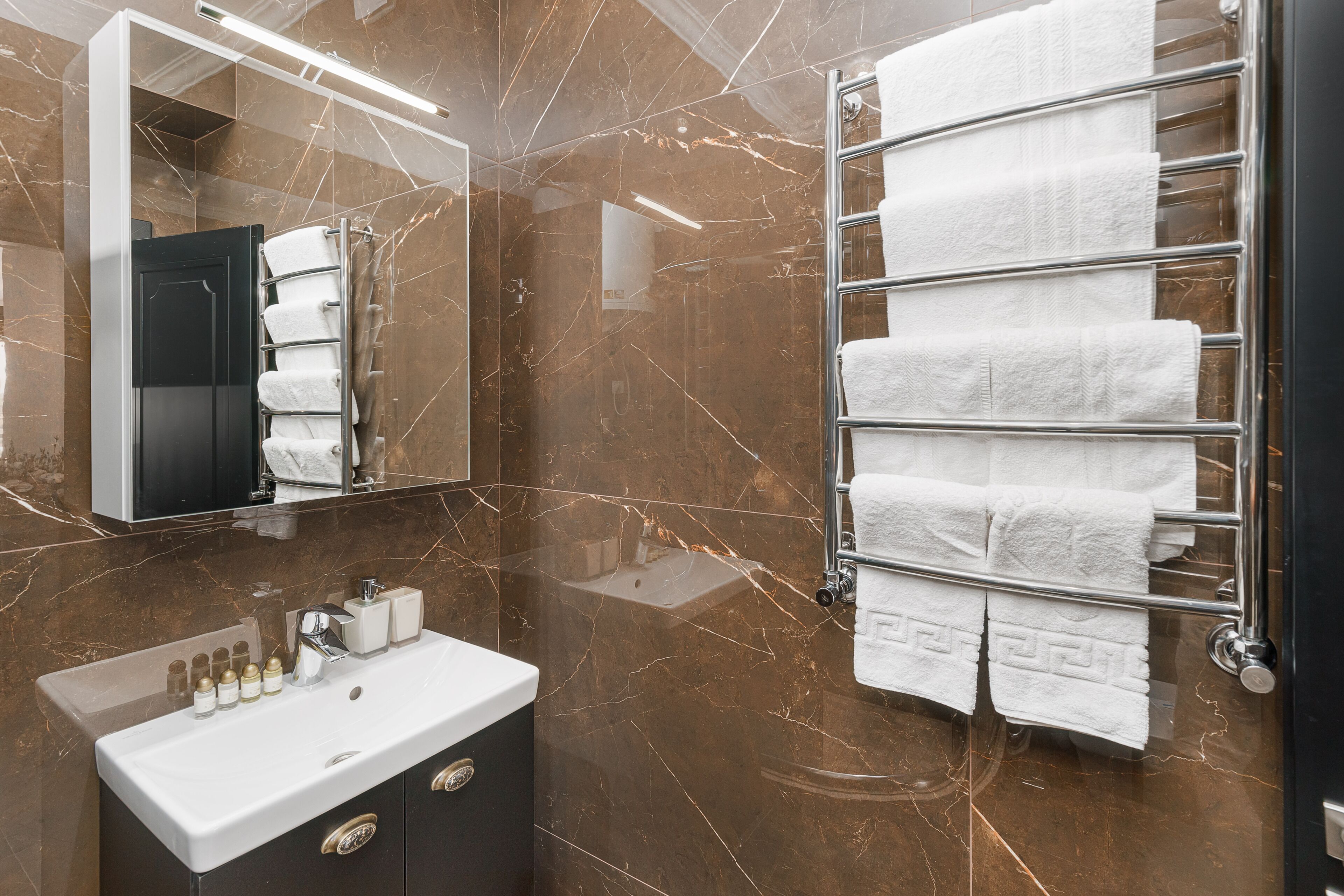 A bathroom with a marble wall, a sink with toiletries, and a towel rack with neatly folded towels.