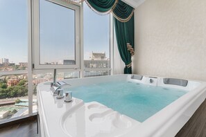 A modern bathroom with a large bathtub, a window with a city view, and a green curtain.