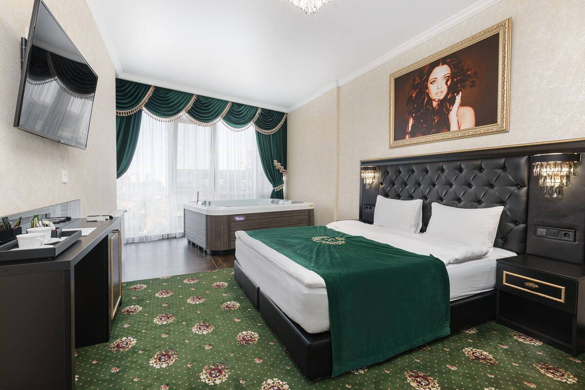 A hotel room with a bed, a desk, a vanity, a bathtub, and a large painting on the wall.