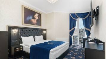 Ein Hotelzimmer mit einem großen Bett, einem Fernseher, einem Schreibtisch und Blick auf die Stadt durch das Fenster.
