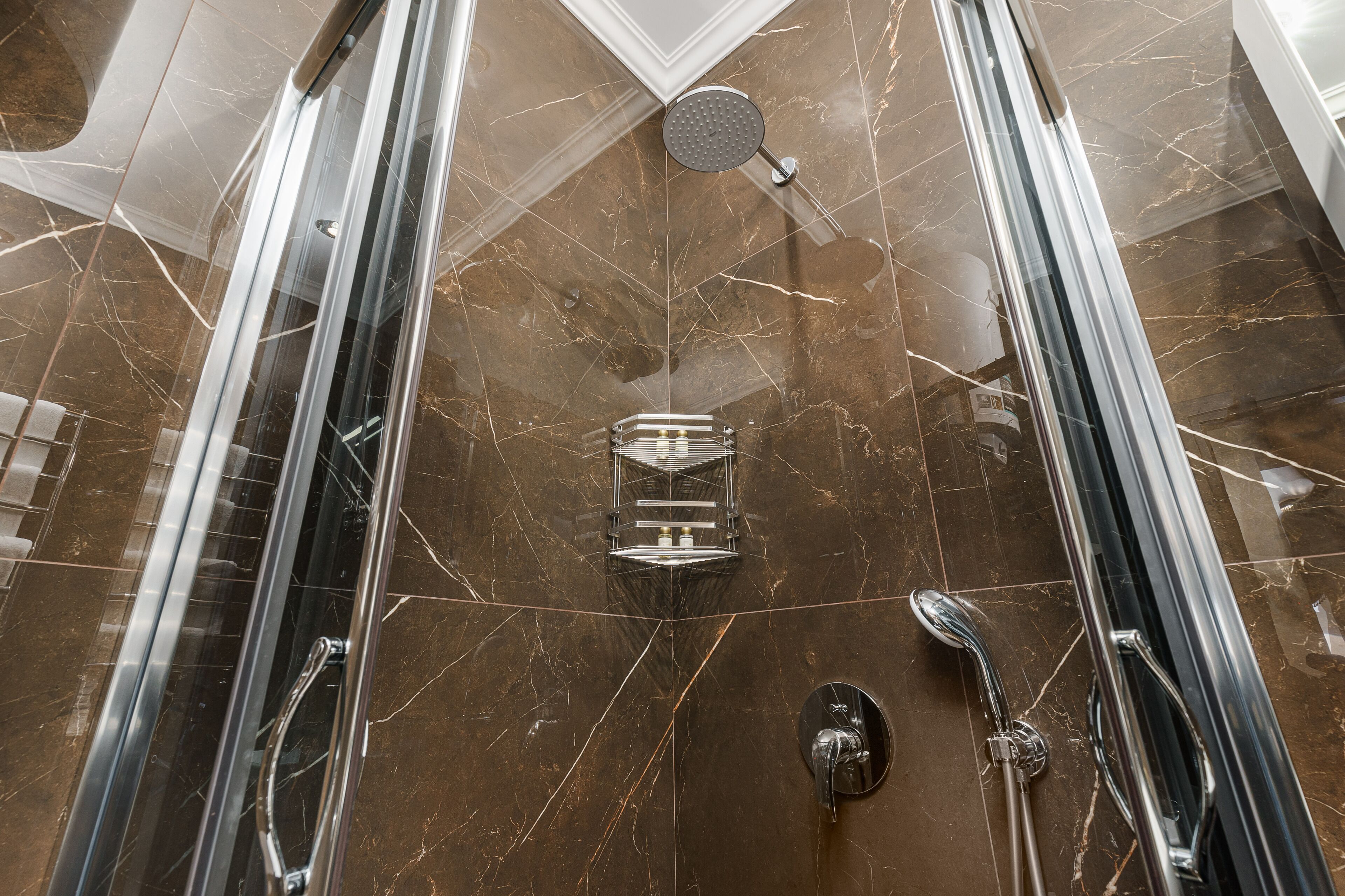 Un baño moderno con ducha, puertas de vidrio y piso de mármol.