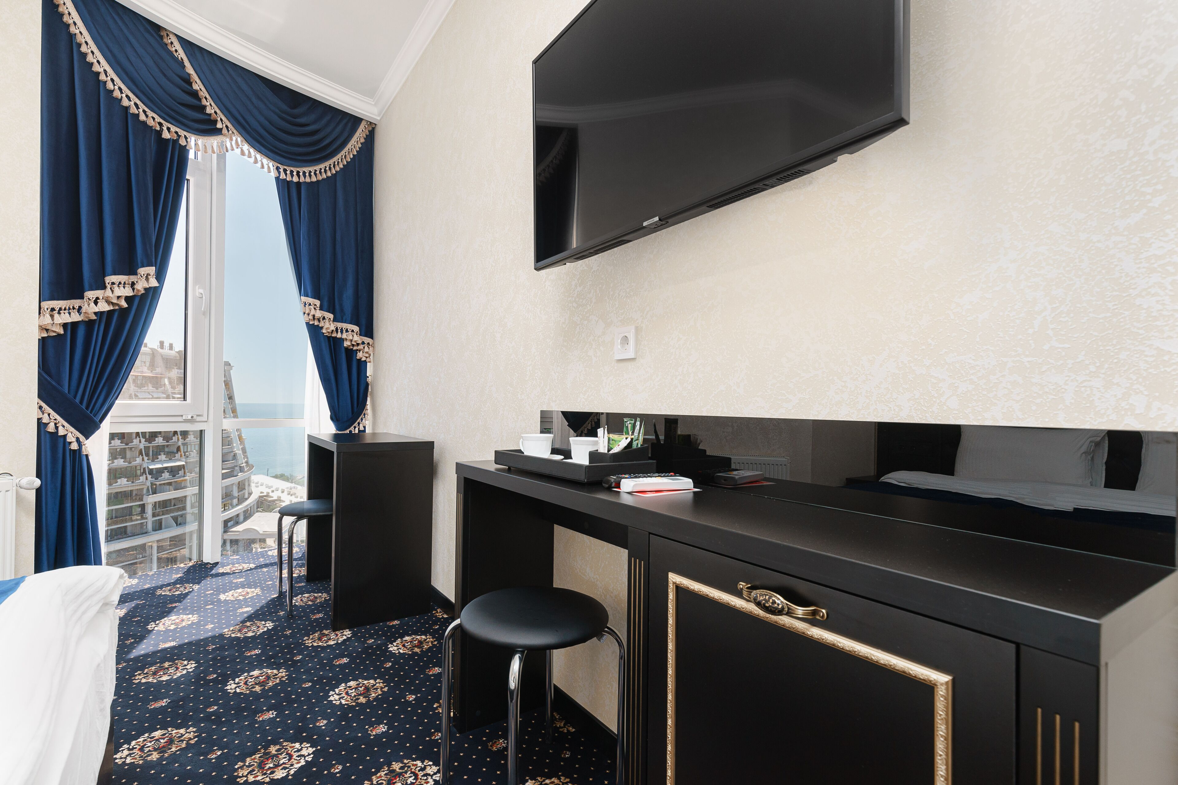 Hotelkamer met een grote televisie, een bureau met stoel, een bed en uitzicht op een gebouw door een raam met blauwe gordijnen.
