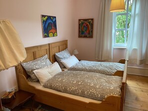 Una cama doble con ropa de cama estampada, un cabecero de madera, una mesita de noche con una lámpara y dos cuadros en la pared.