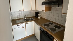 A compact kitchen with white cabinets, a stainless steel sink, a coffee maker, and a stove.