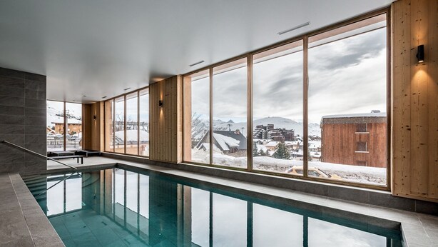 Una piscina interior moderna amb grans finestres que ofereixen vistes a un paisatge nevós i edificis.