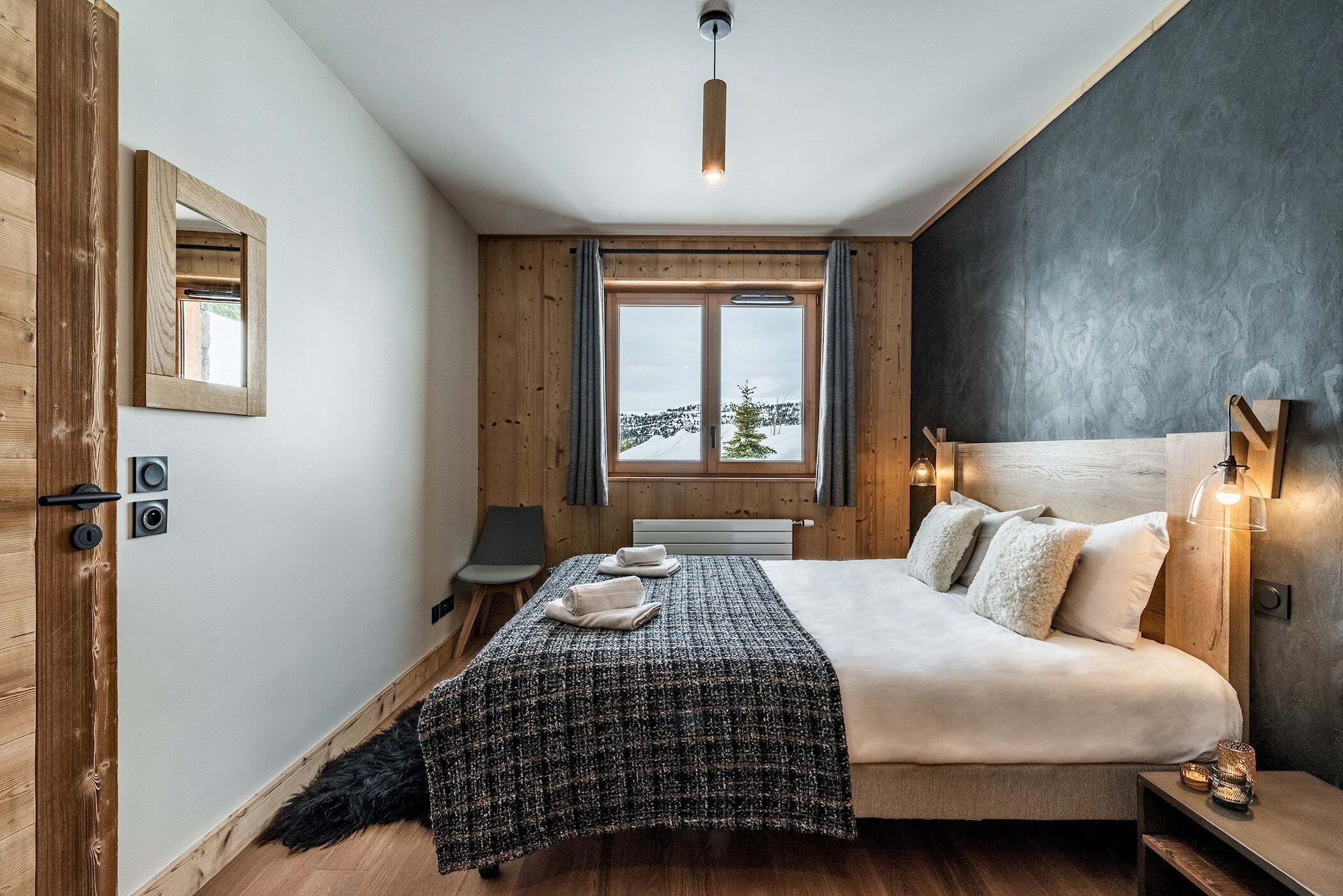 A bedroom with a large bed, a mirror, a window with curtains, and a view of the outdoors.