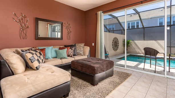 A living room with a sofa, ottoman, and a glass door leading to a pool area. - Windsor Palms-ru556 (Kissimmee)