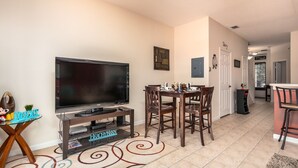 A living room with a TV, a dining table, and chairs. There is a small table with toys and a sign that says "RESORT". - Windsor Palms-ru556 (Kissimmee)
