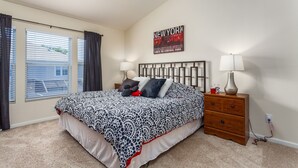 A bedroom with a bed, two bedside tables, a wall clock, a poster, and a window with curtains. - Windsor Palms-ru556 (Kissimmee)
