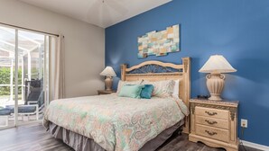 A bedroom with a large bed, two bedside tables with lamps, a blue accent wall, and a view through a glass door. - Tuscan Hills-ru1064 (Davenport)