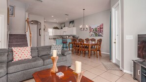 A living room with a gray sofa, wooden coffee table, and a dining area with wooden chairs and a blue tablecloth. - Tuscan Hills-ru1064 (Davenport)