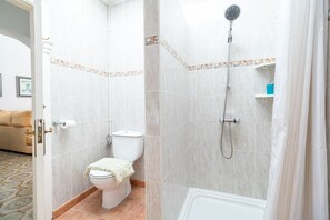 A bathroom with a toilet, shower, and a small shelf with toiletries.