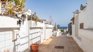 Une rue étroite aux murs blancs, une plante en pot et une vue dégagée sur la mer.