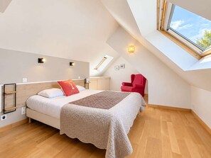 A bedroom with a sloped ceiling, a skylight, a bed with a quilt, a red chair, and a bedside table.