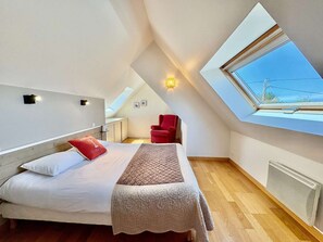Een slaapkamer met een bed, een rode stoel, een dakraam en een radiator.