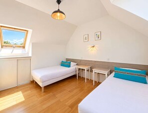 Une chambre avec deux lits, une lucarne, une petite table et un luminaire fixé au mur.