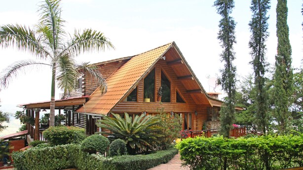 Un chalet en bois doté d’un toit à pente, entouré de jardins bien entretenus et de grands arbres.