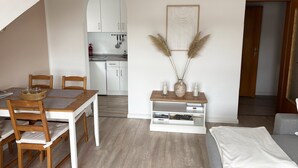 Una sala moderna con comedor, una cocina al fondo y una estantería con adornos.