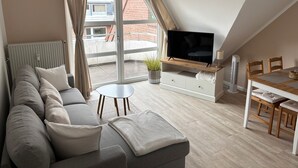 Una sala de estar moderna con sofá, televisor, mesa de comedor y vista a un edificio de ladrillo a través de un ventanal grande.