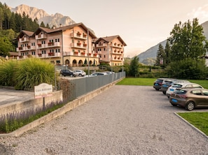 A hotel with multiple balconies, a gravel driveway, and parked cars. - LA CANONICA nature and peace, with terrace Wi-Fi PetFriendly with dog area (Baselga di Piné)