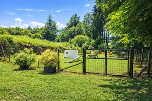 A fenced garden area with a sign, a small bridge, and a playground in the background. - LA CANONICA nature and peace, with terrace Wi-Fi PetFriendly with dog area (Baselga di Piné)